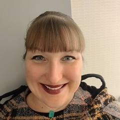 Woman with brown bangs, wearing makeup and smiling