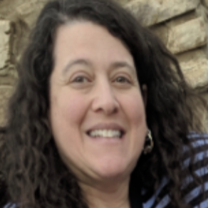 Woman with dark curly hair smiling and looking at the camera. She wears a blue and white striped shirt.