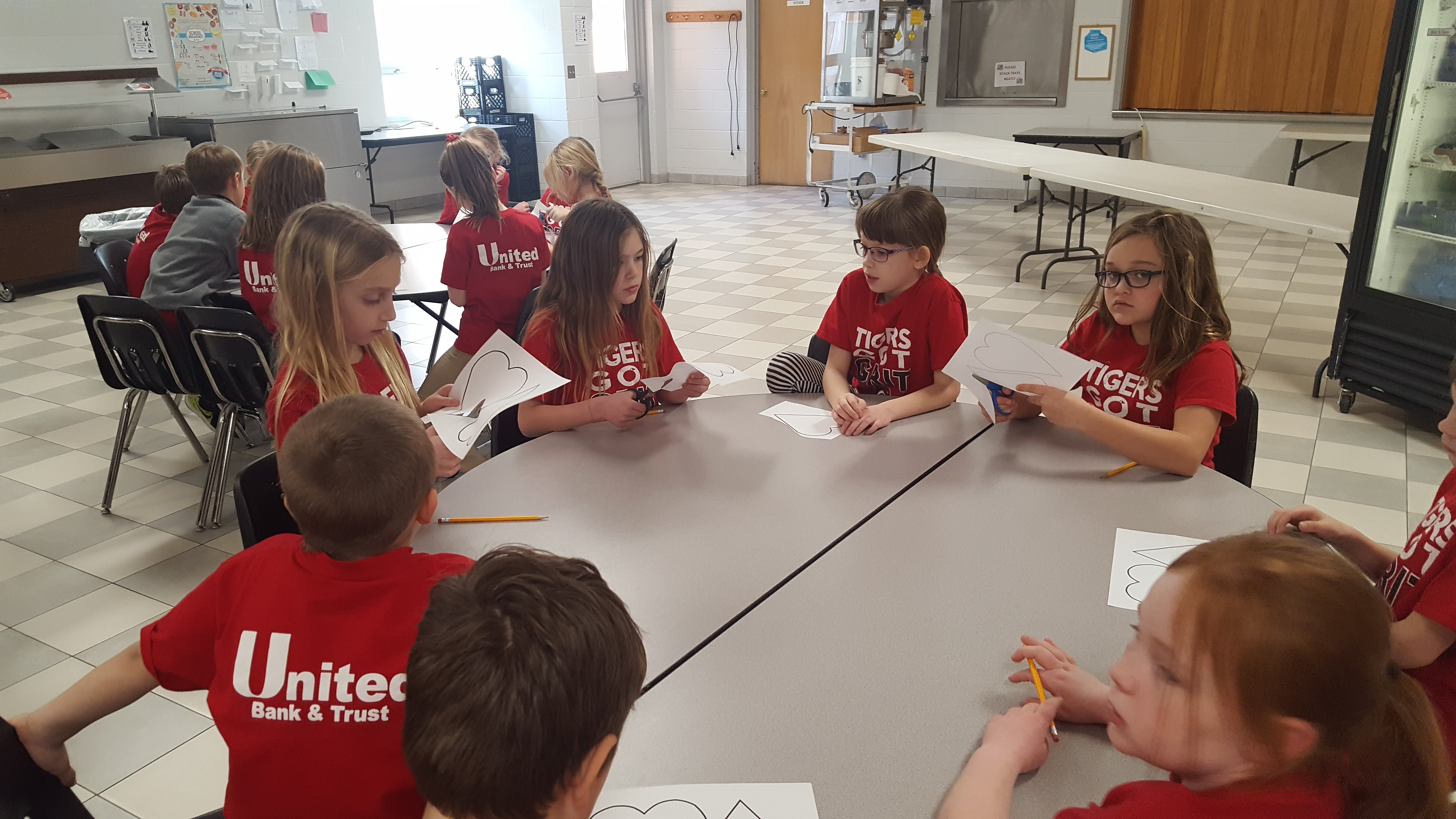 Group of children all together across a table and cutting paper shaped hearts.