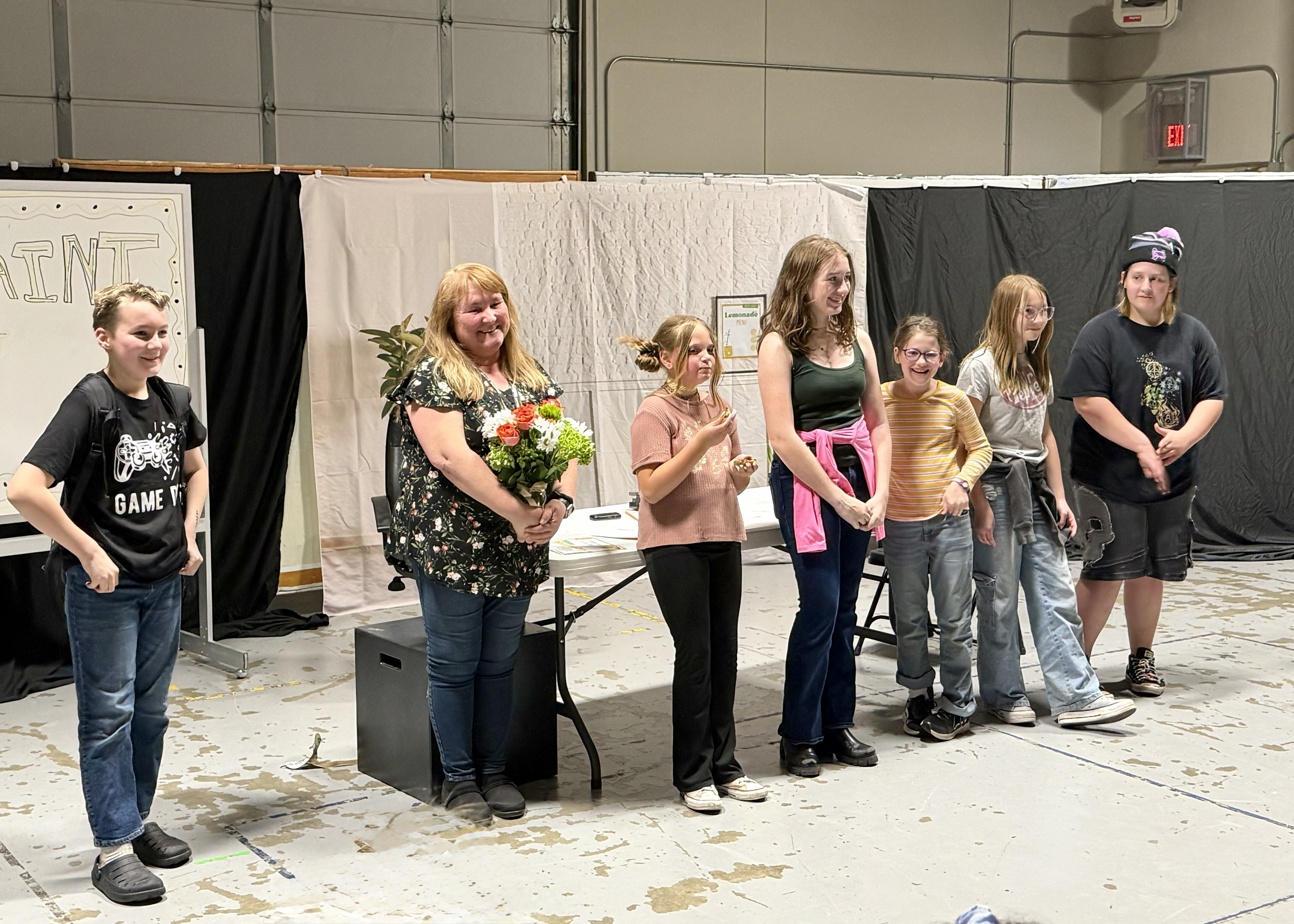 A group of people stand together in a room, with a woman holding a bouquet of flowers.