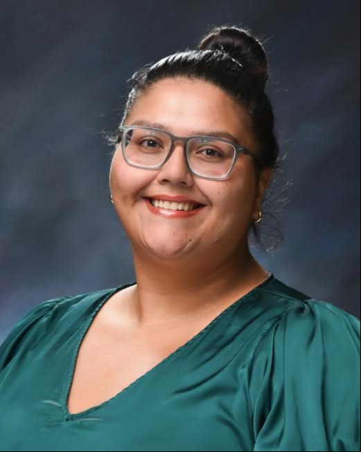 Portrait of a Kaitlyn Hernandez wearingglasses and a green top against a dark background.