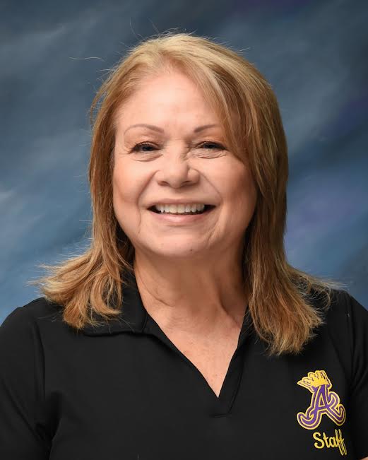 Smiling Roxana Santiago wearing a black polo with a logo, set against a blue gradient background.