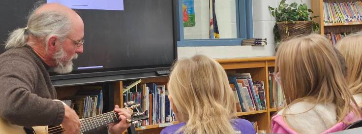 Board Member playing a guitar to students in a classroom