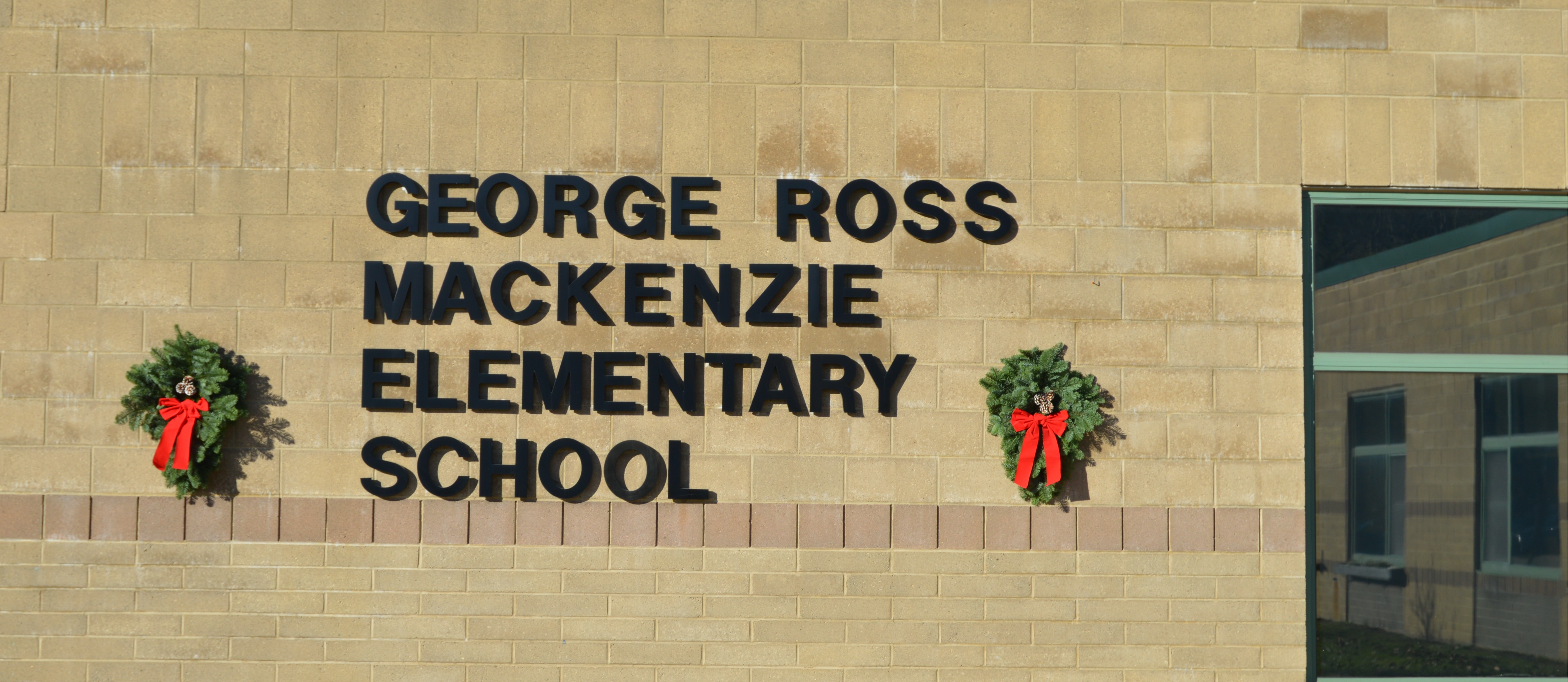 George Ross Mackenzie Elementary School main entrance decorated with 2 green wreaths with pine cones and red bows