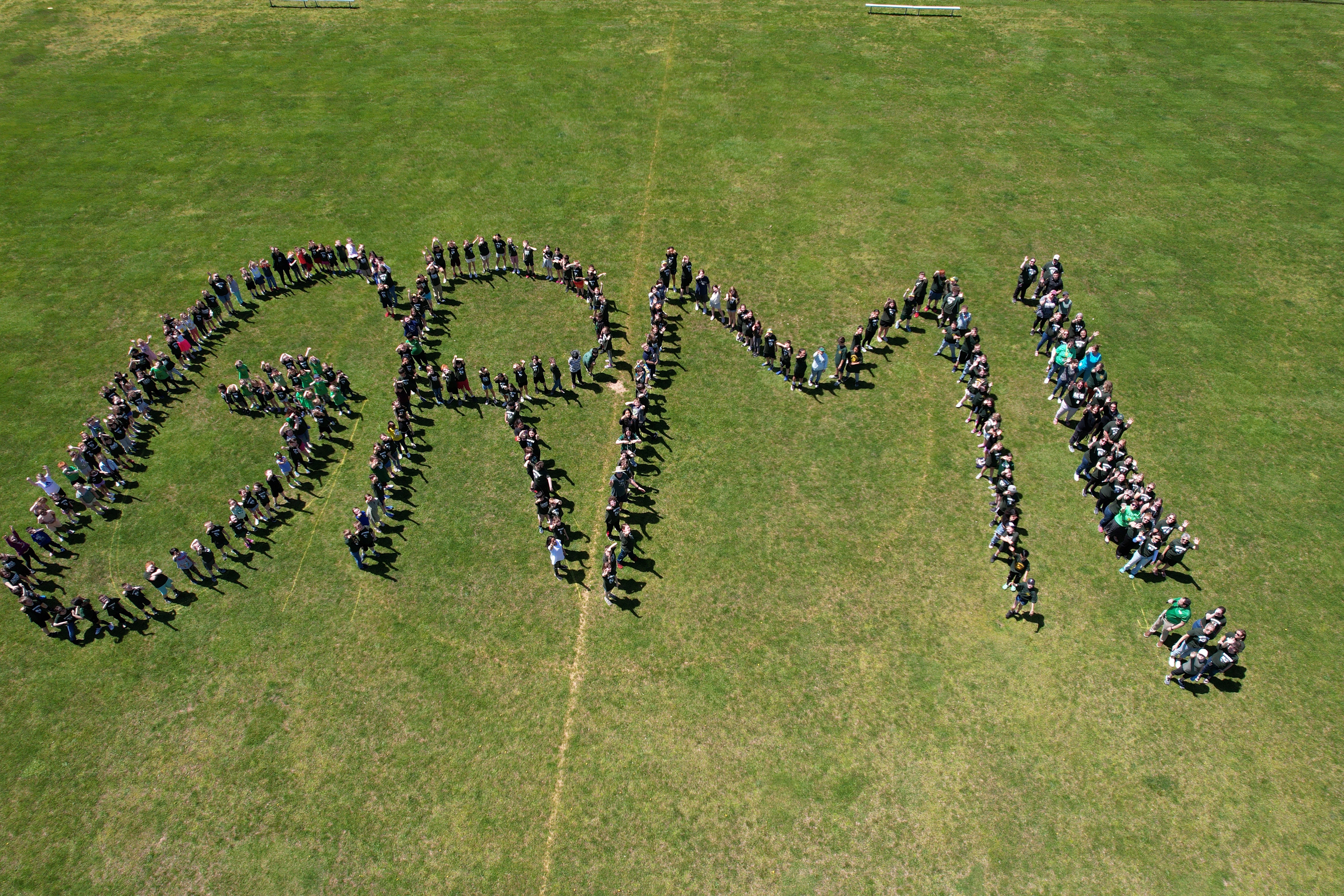 Arial image of students and staff standing in the formation of the letters GRM! on a green field.