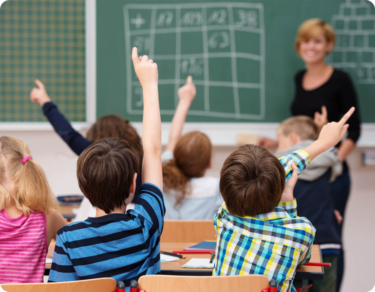 6 students raising hand in class 1 teacher in front of blackboard