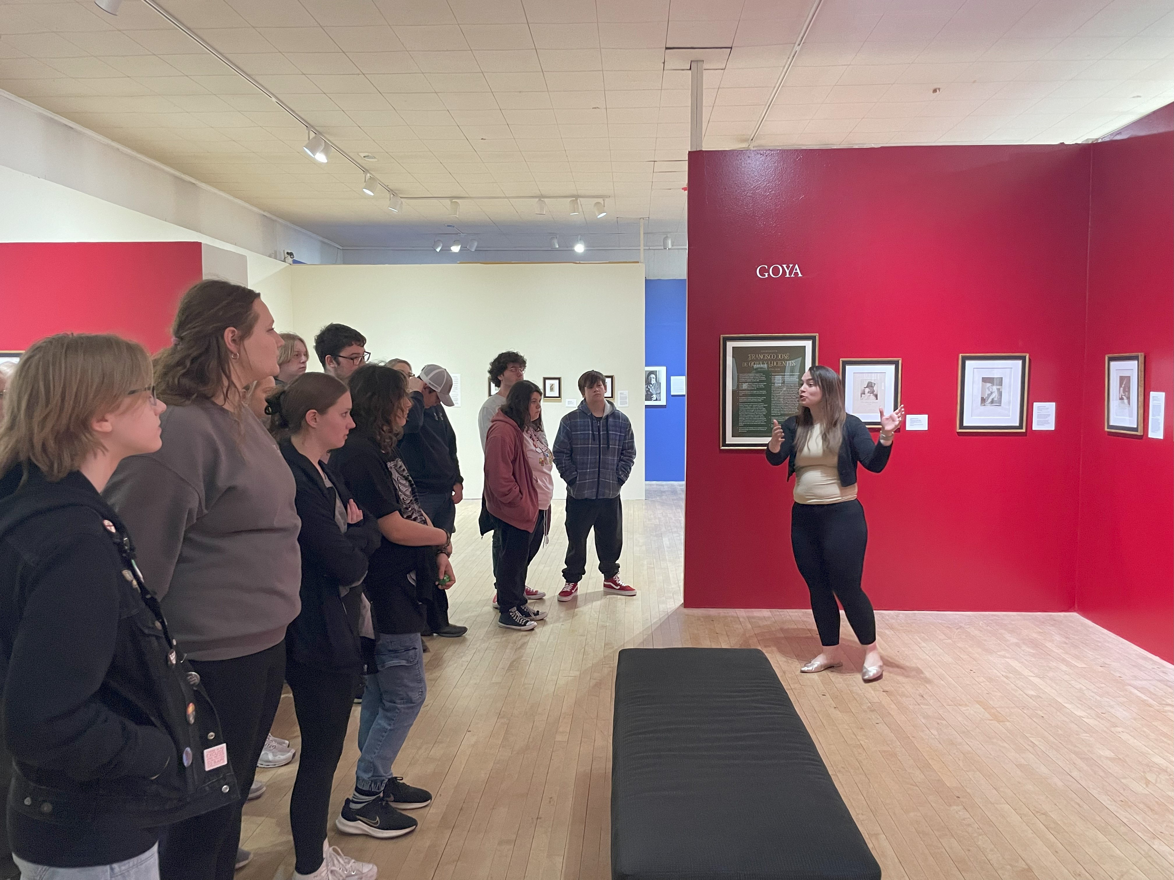 students line on the left, observing a wall of art pieces being introduced by an art museum employee