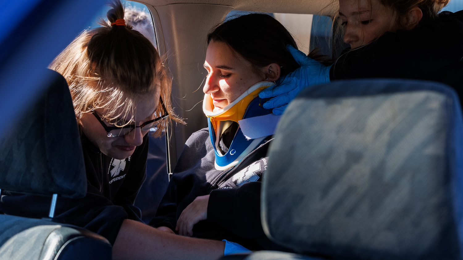 EMT students putting a neck brace on a student in the backseat of a car.