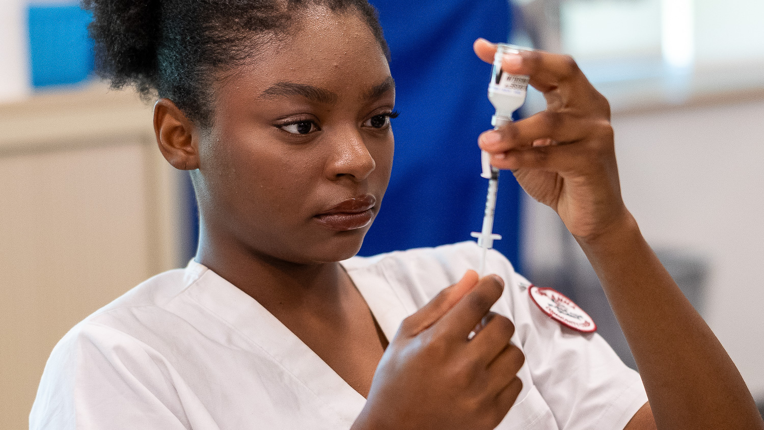 Healthcare Technician student using a syringe to draw medicine from a glass vile.