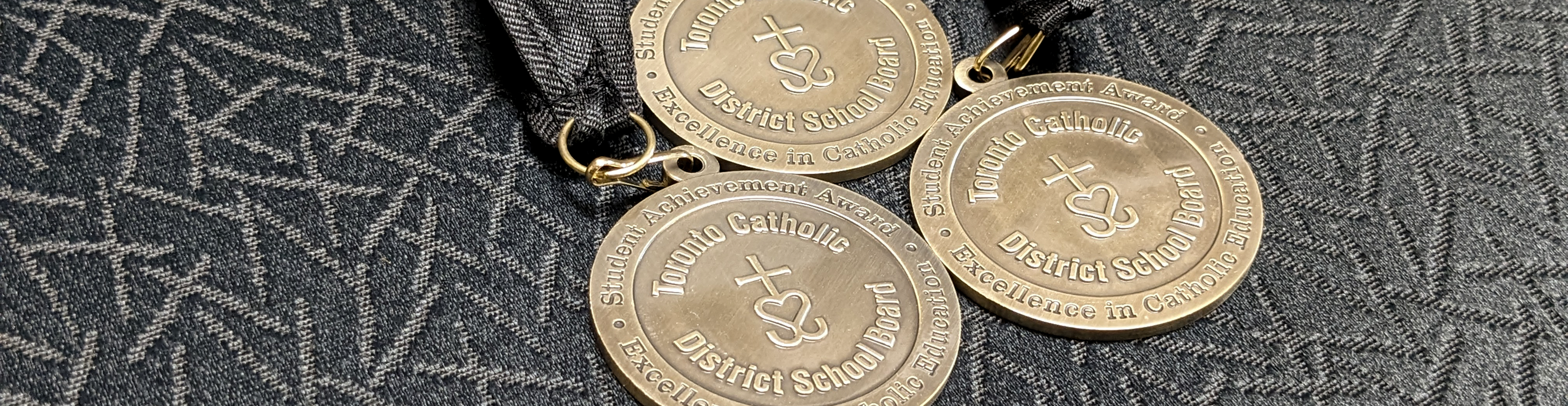 Photo of three TCDSB Student Achievement Award medals lying on a grey fabric background.