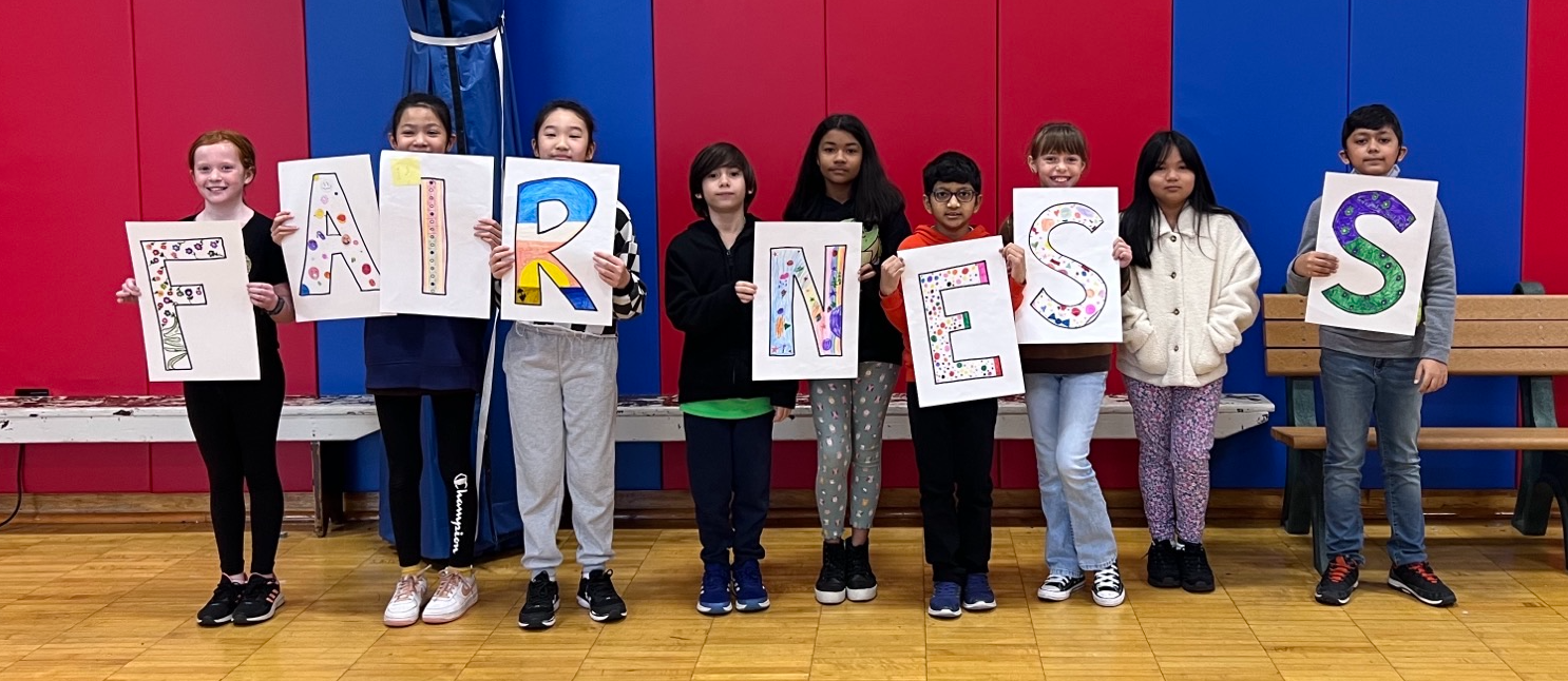 8 students standing with posters that spell out FAIRNESS