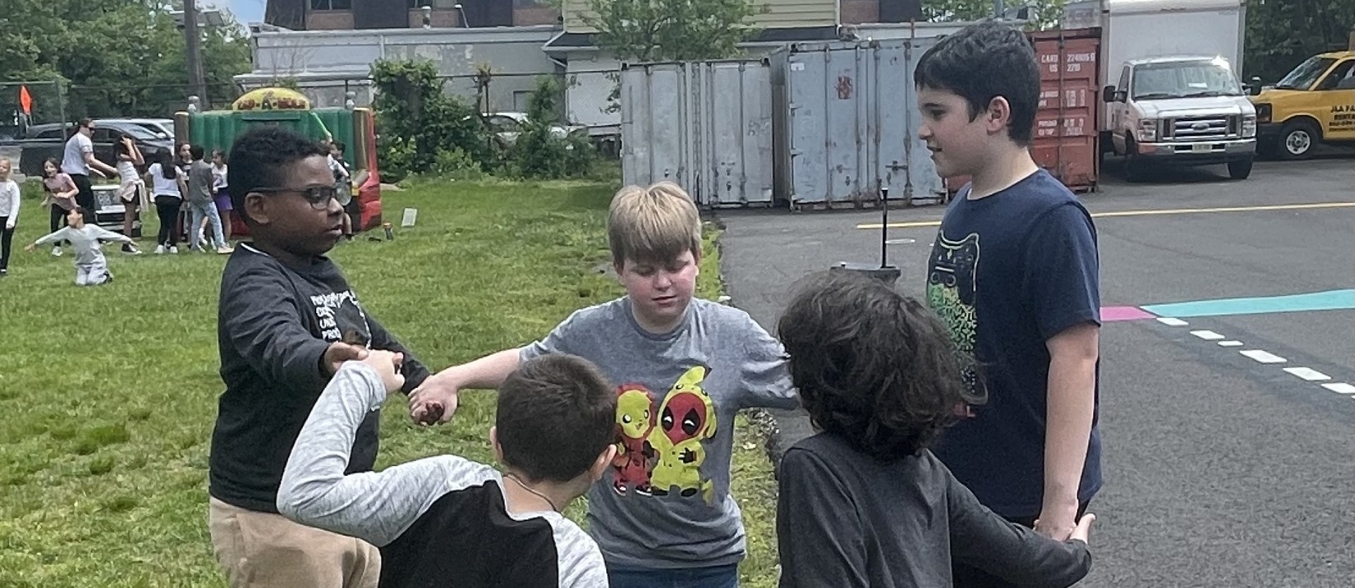 students holding hands playing ring around the rosie outside on school grass