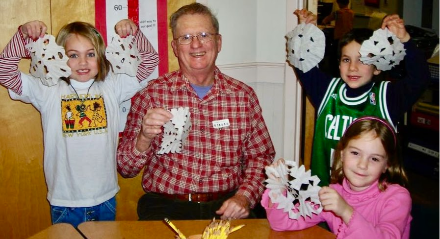 Volunteer Jack Foster with younger students working on cutting snow flakes.