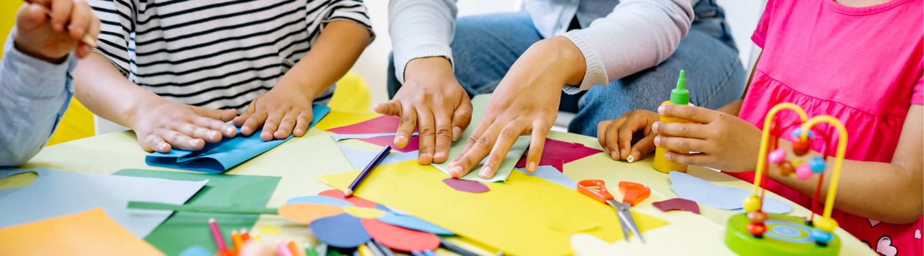 Close up of an arts and crafts table and young students folding construction paper