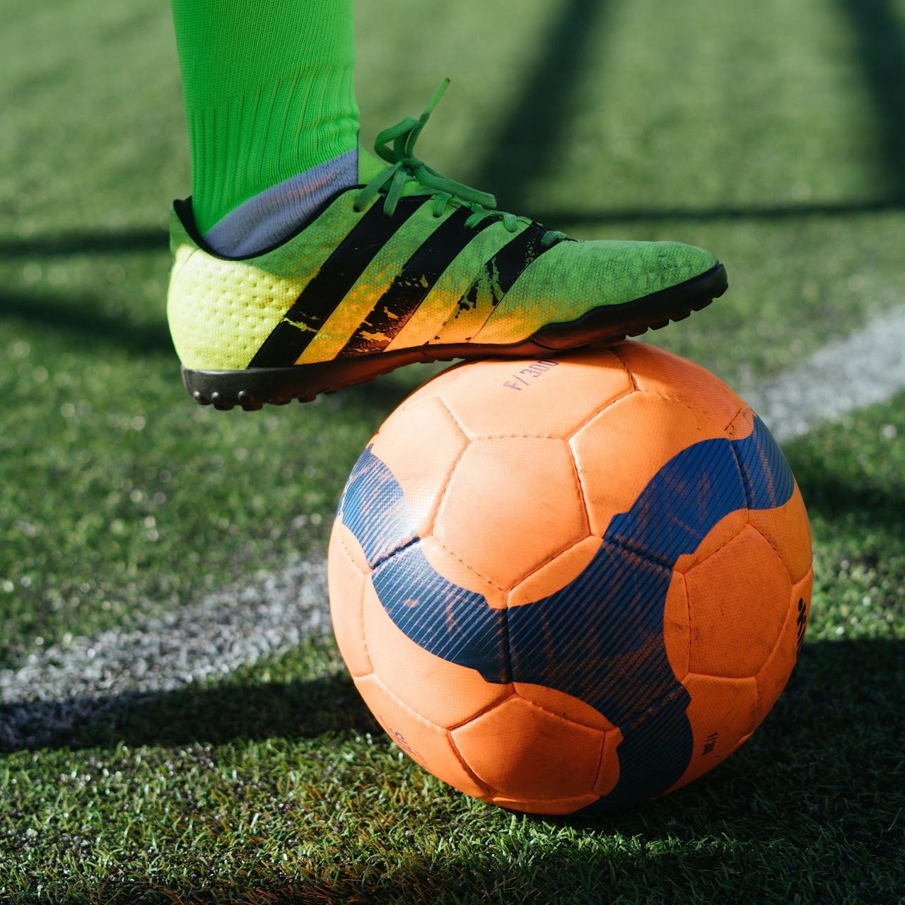 A foot wearning a soccer shoe  on top of a orange soccer ball