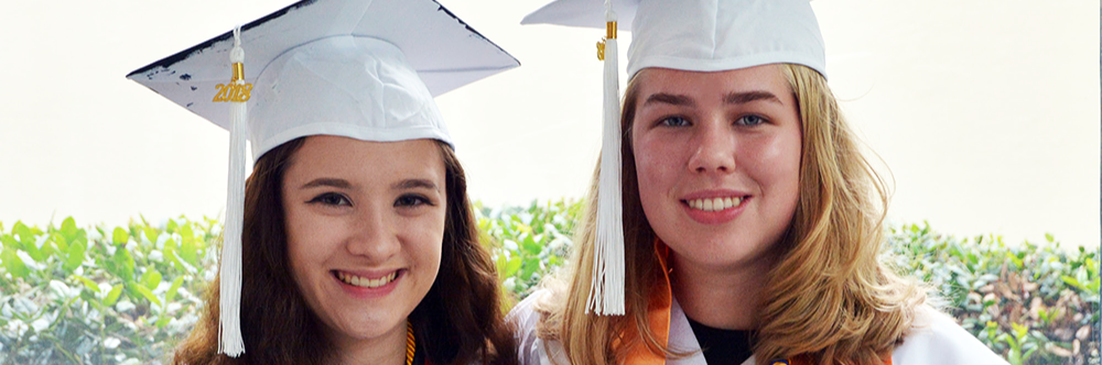 Two teenagers wearing white graduation gown and cap