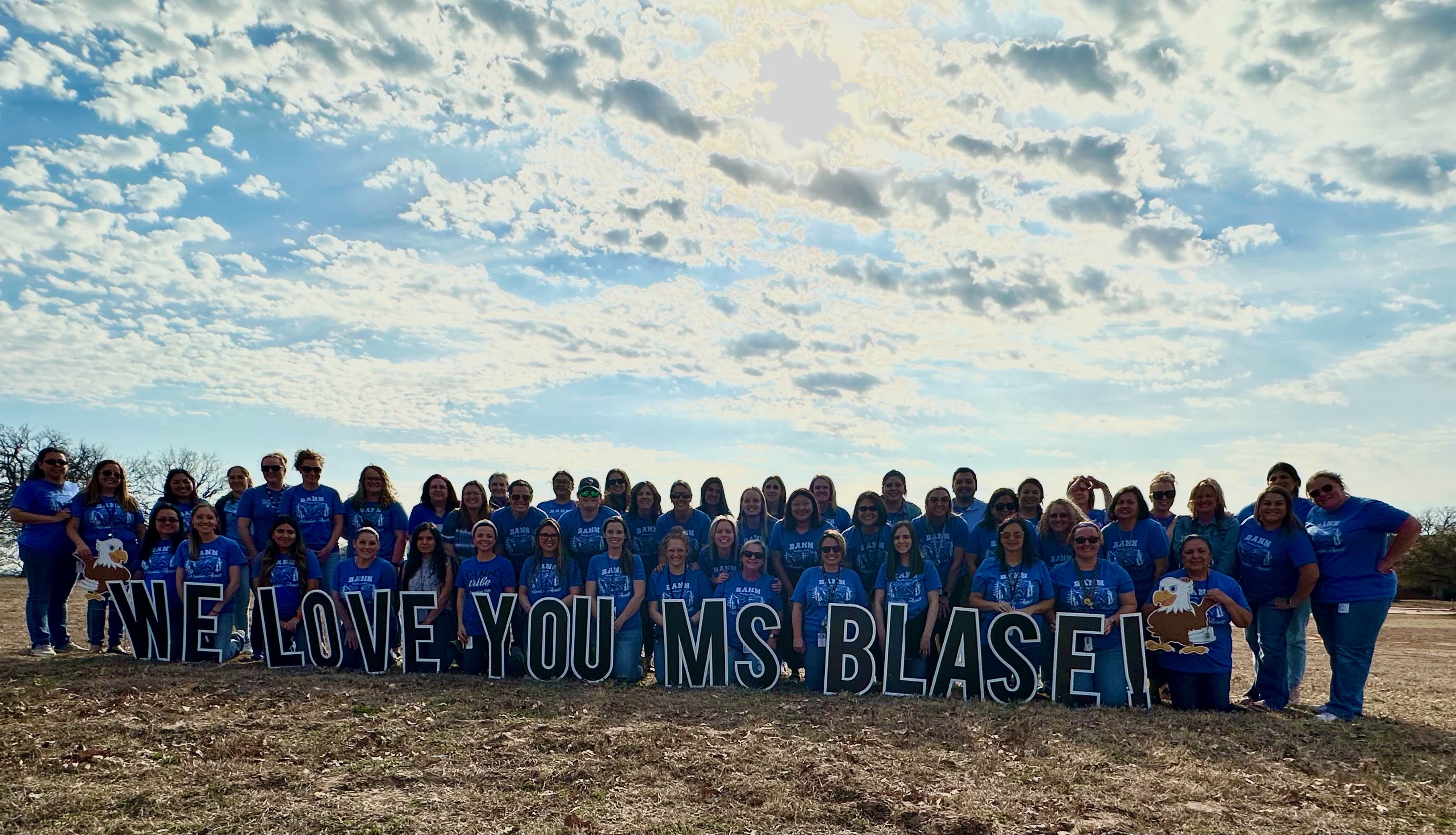 rann staff wearing blue shirts standing in front of the We Love You Ms. Blase yard sign