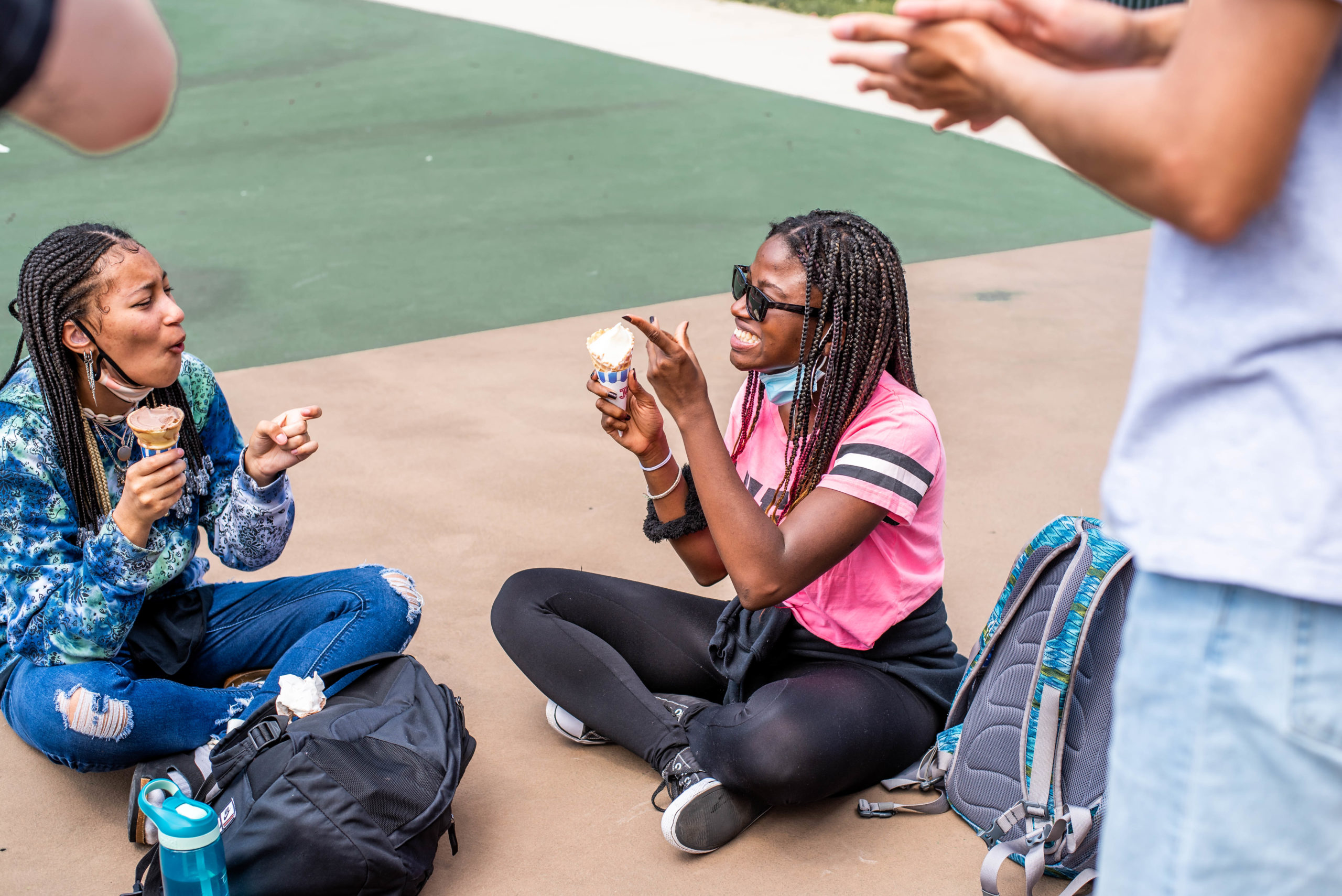 2 students sitting on the ground outside at an ice cream social