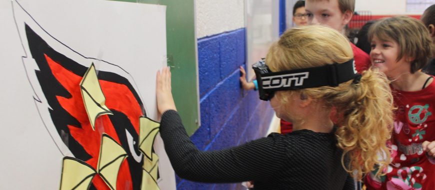 A student with black-out goggles on trying to put the beak on the cardinal similar to pin the tail on the donkey