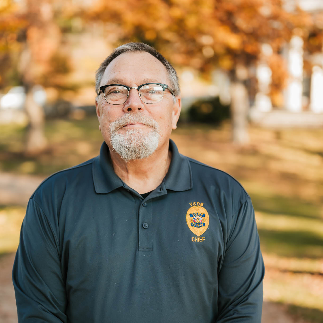 Charlie Coker in his police uniform with glasses and trees in the background