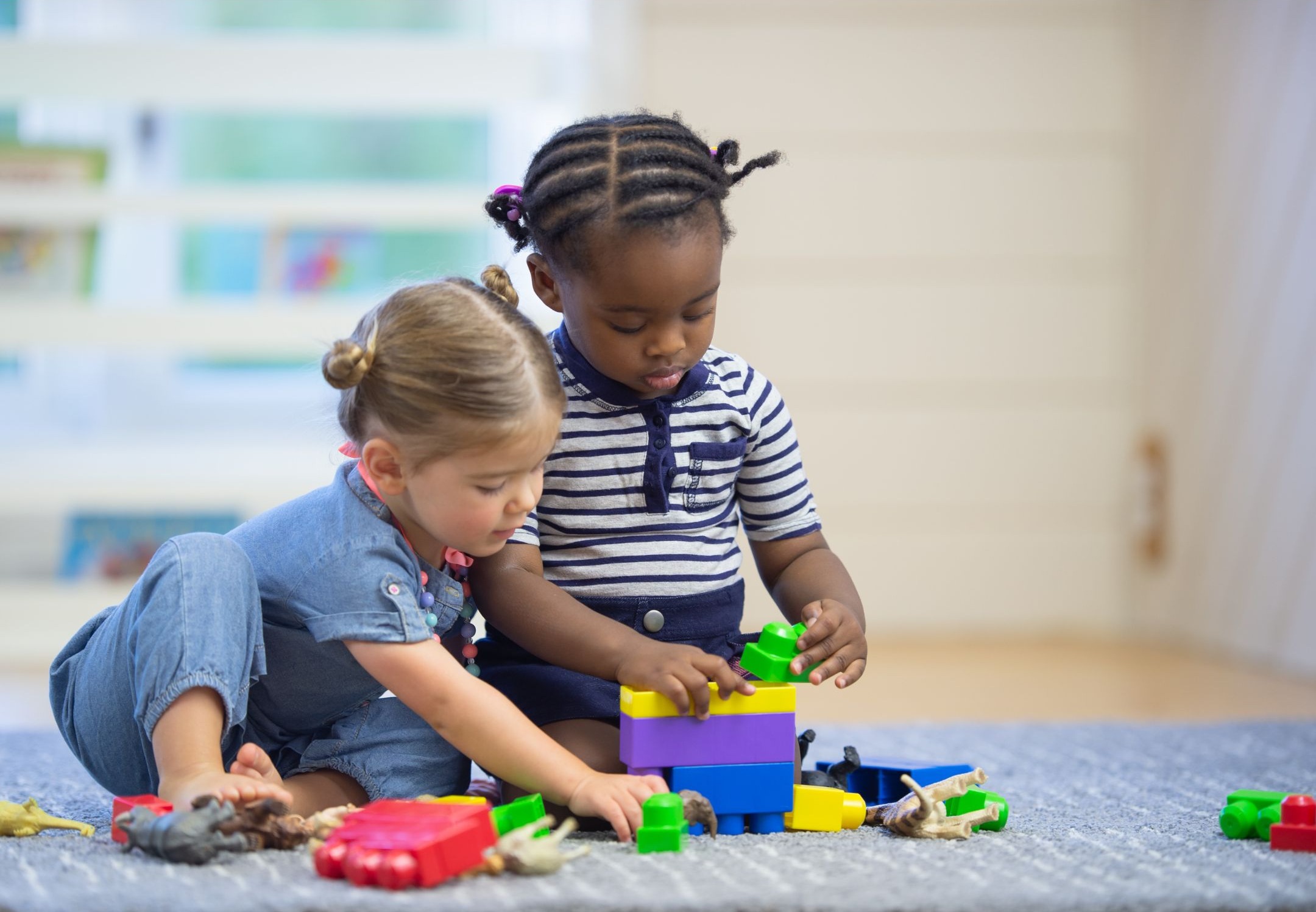 two toddlers building with plastic blocks