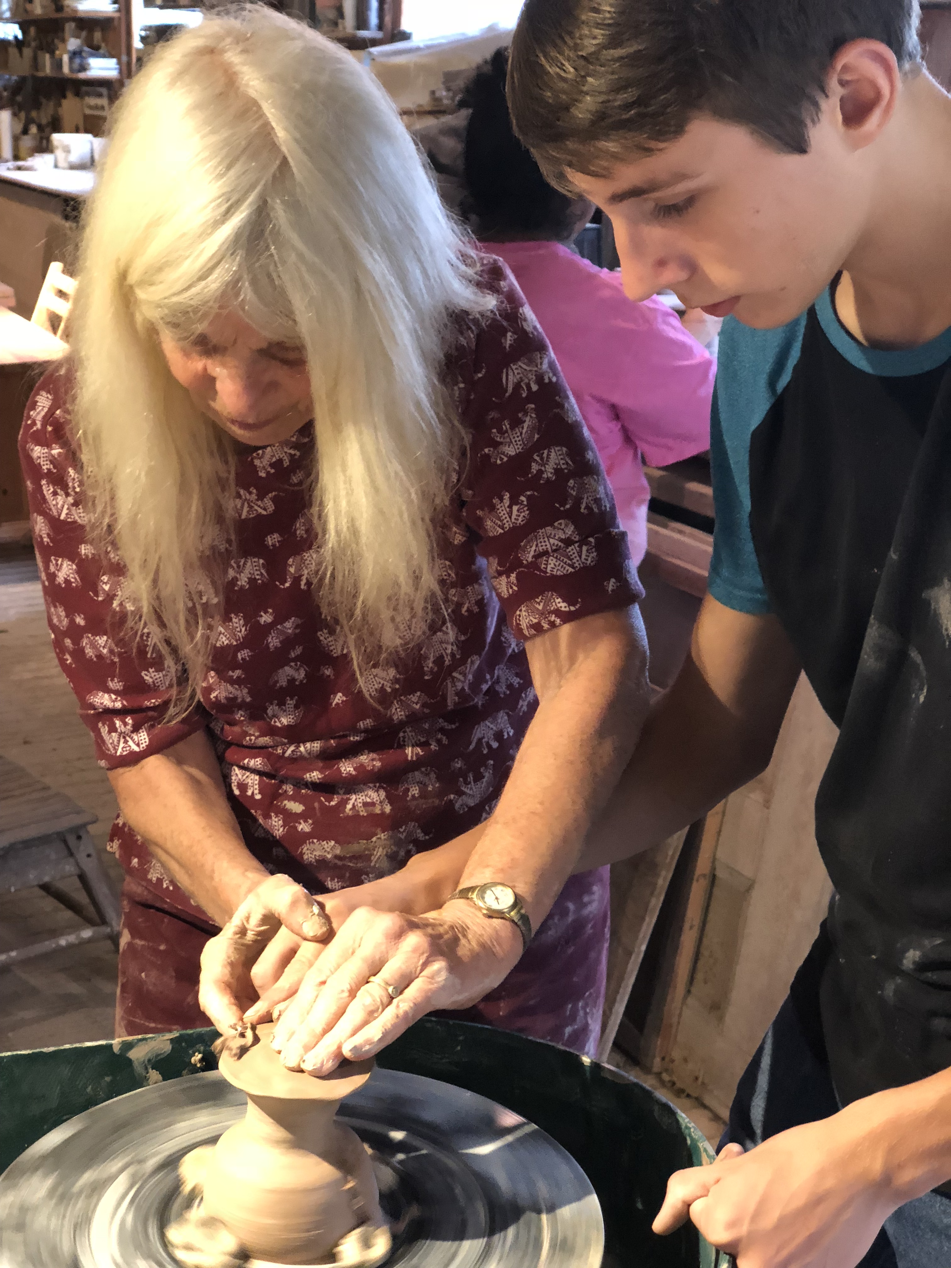 Teacher assisting student with sculpting pottery