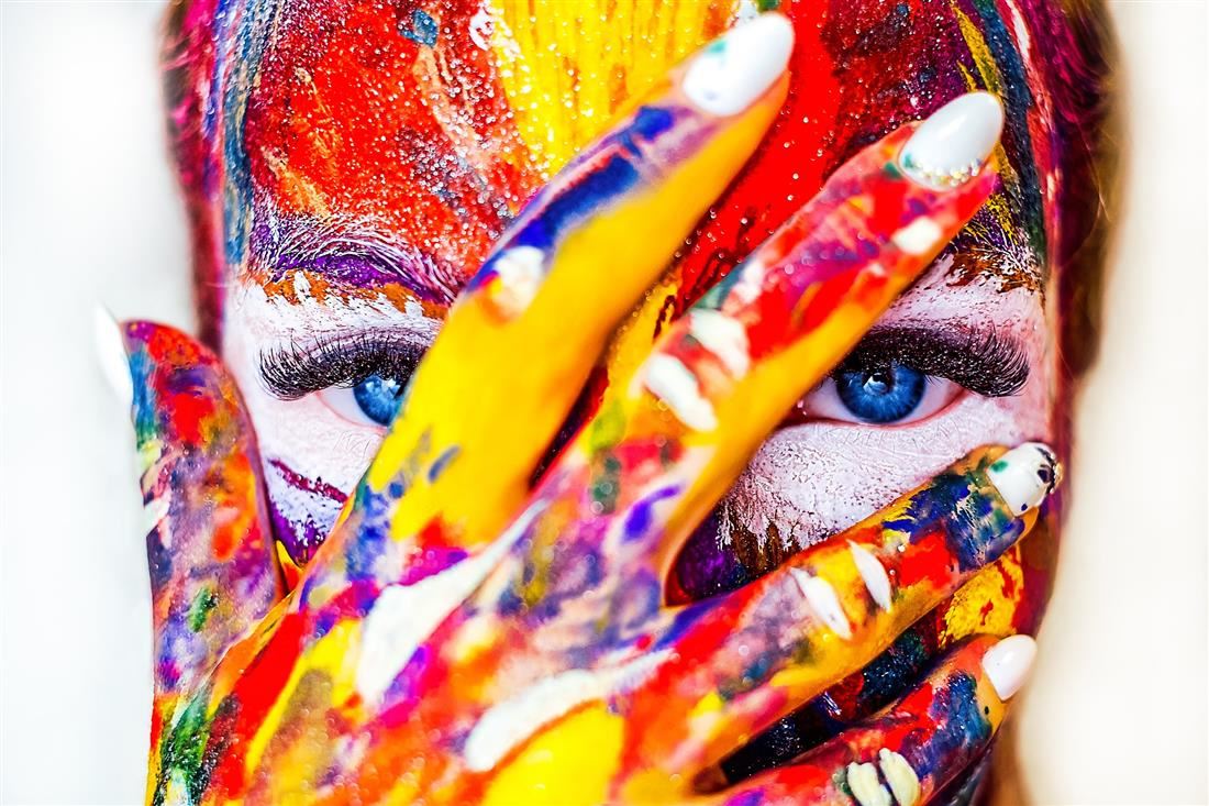 An artful photo of a woman covered in paint while covering her face with her hand