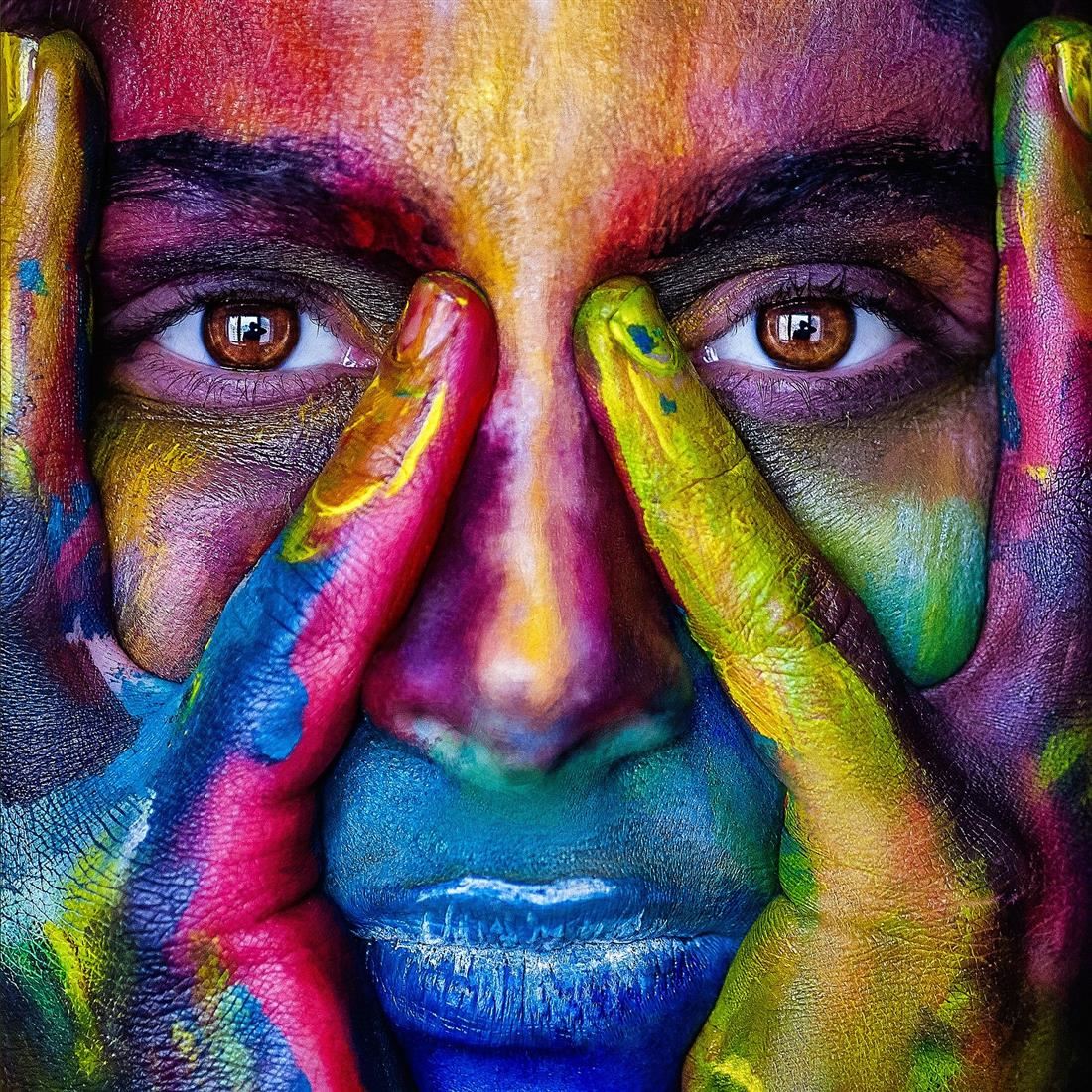 An artistic photo of a woman's face and hands painted many colors