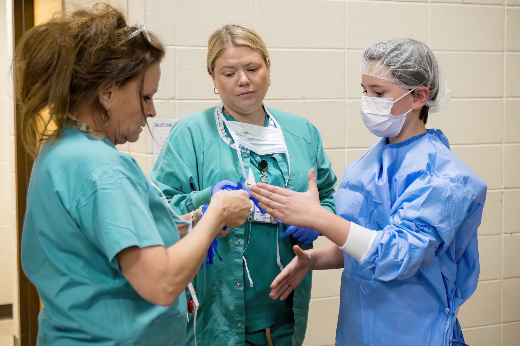 two nursing staff helping student put on surgical scrubs