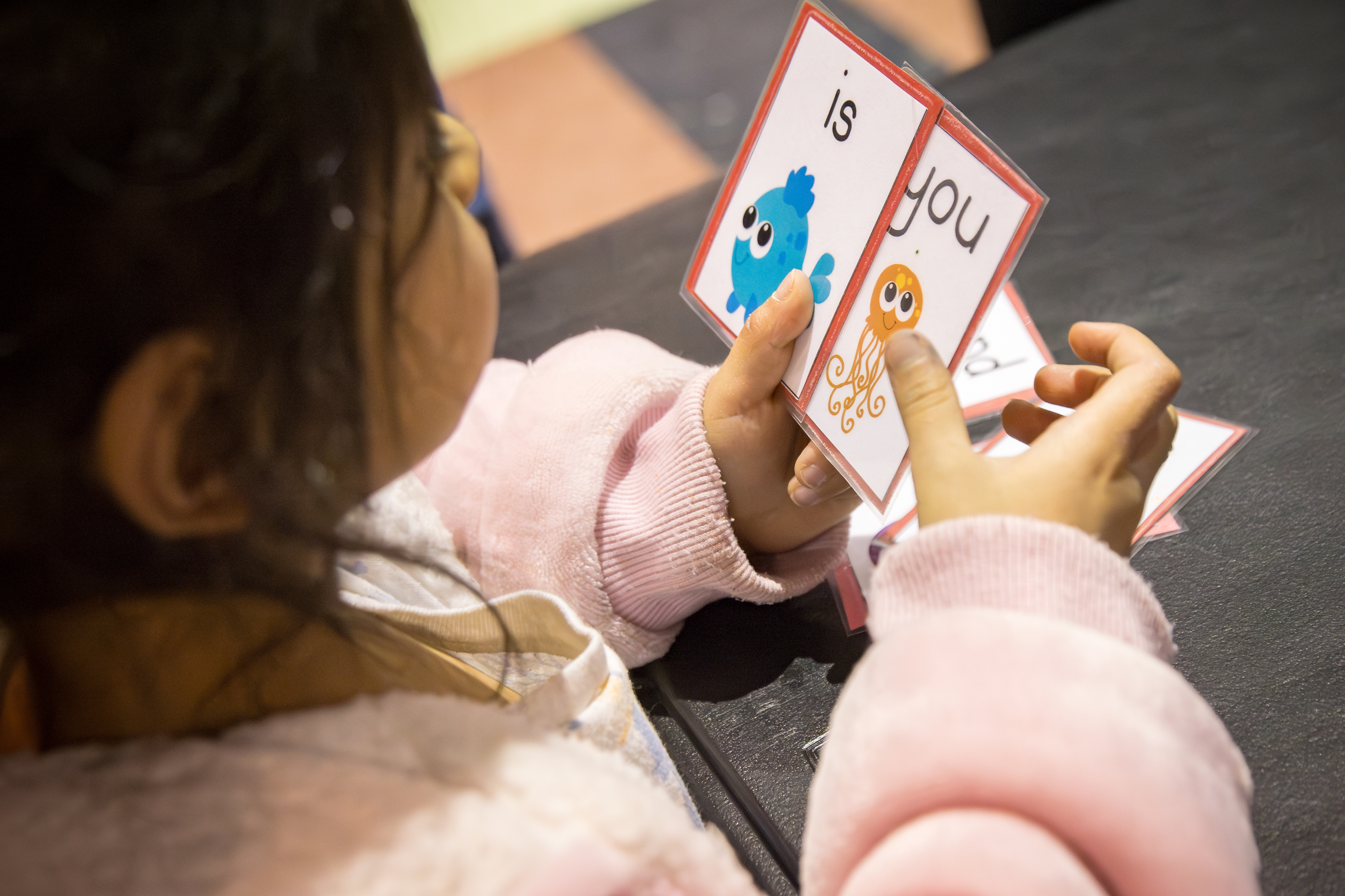 kindergarten student holding flashcards with short learning words on them.