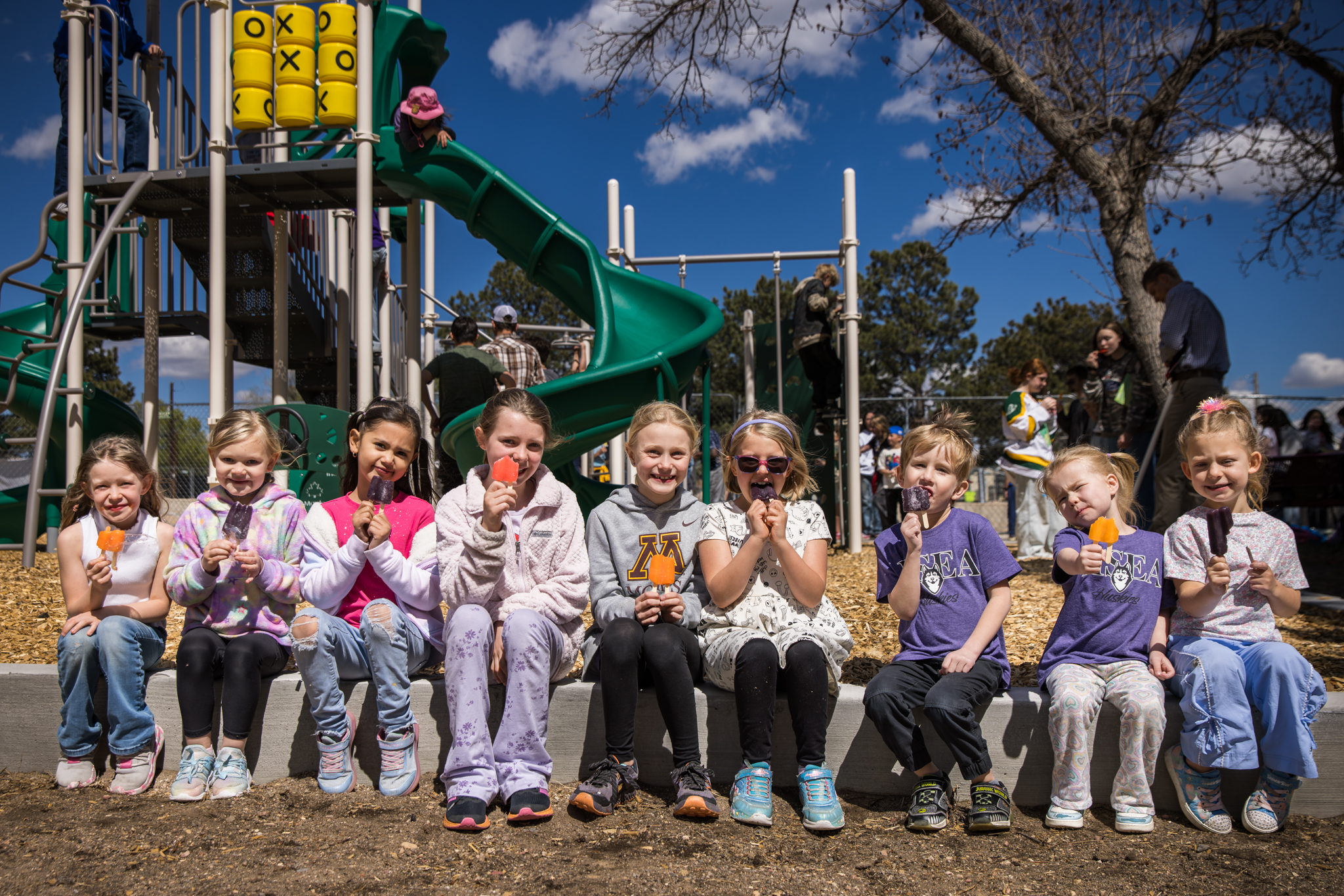 HSEA students sitting in a line while eating popsicles in front of the new hsea playground