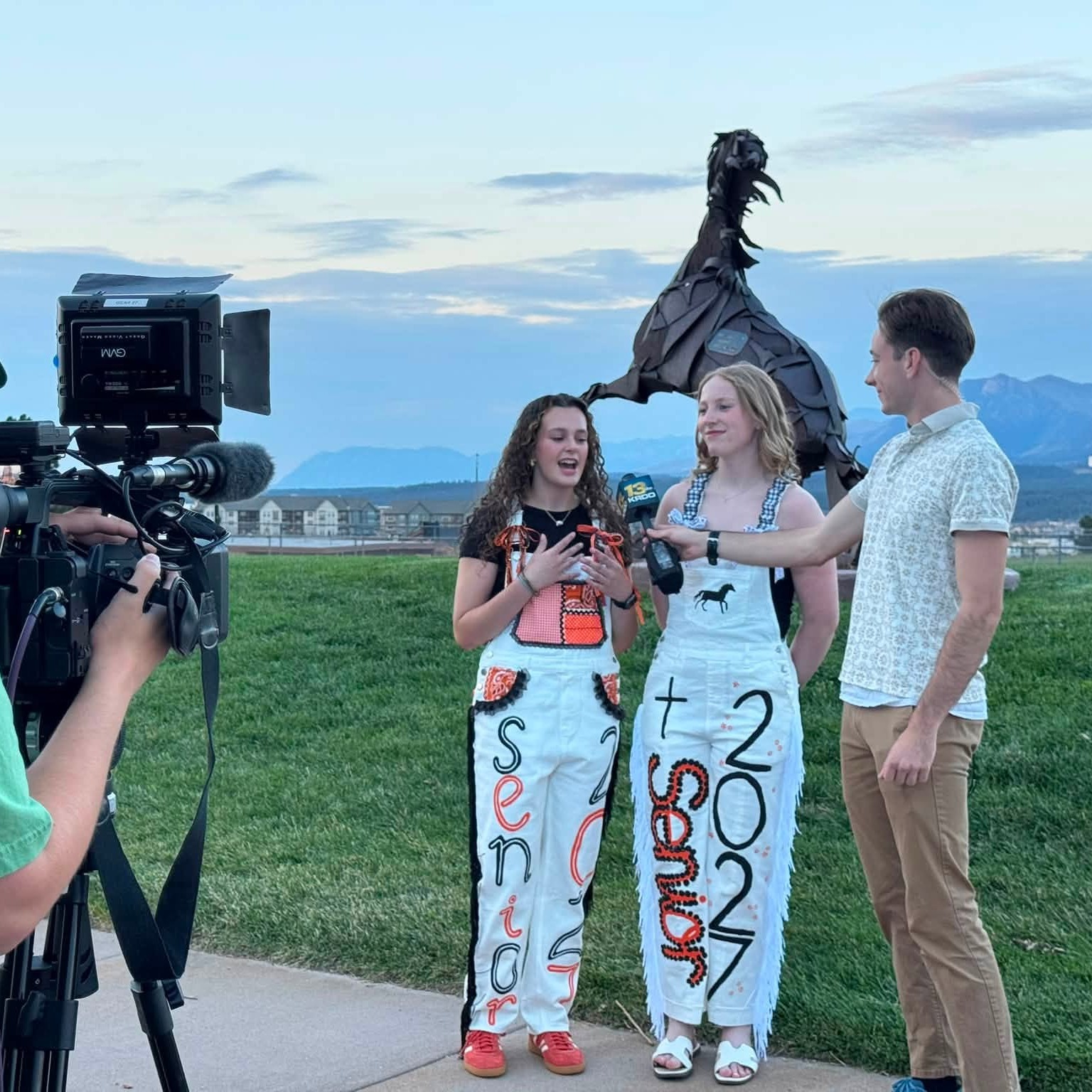 Two LPHS senior girls talk to a news reporter in front of the horse statue