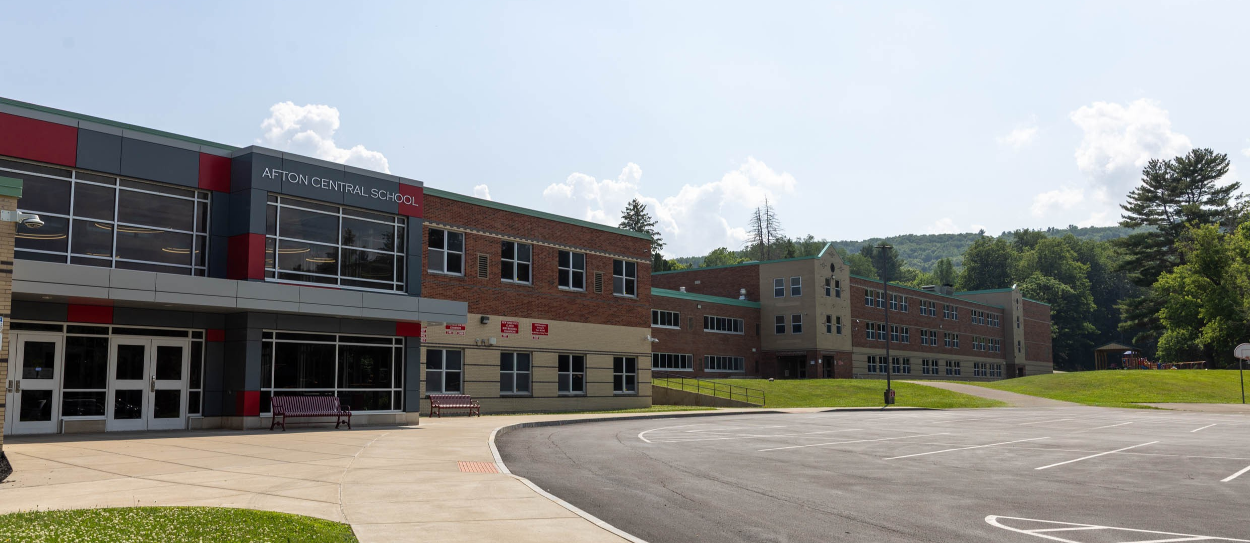 School building entrance, driveway, and a basketball court. Large parking lot in front.