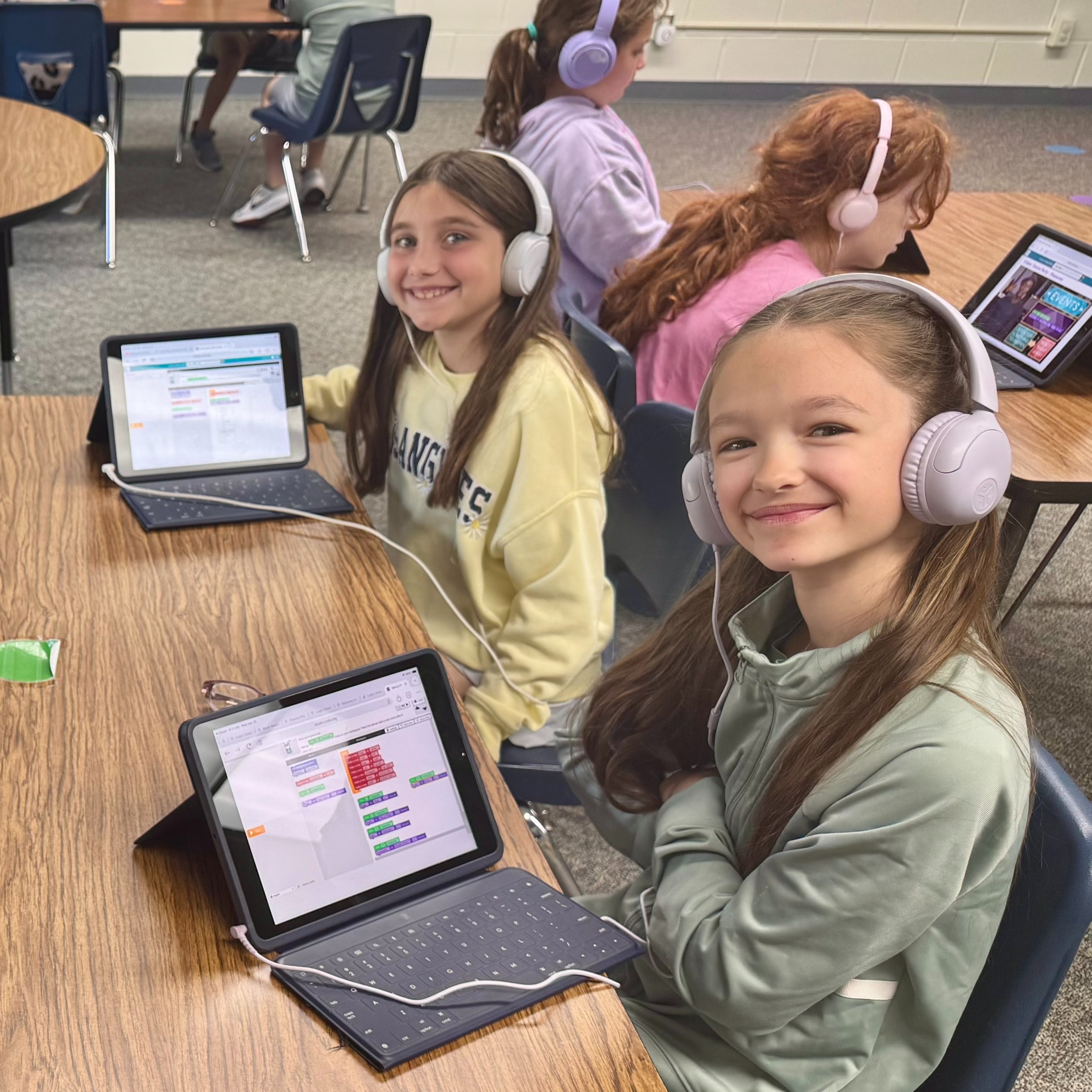 Students sitting at tables with ipads working on a coding application wearing headphones plugged into each ipad