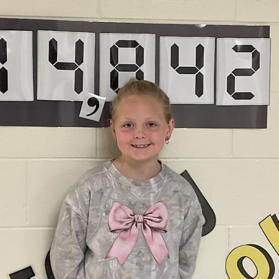 Reese - West Elementary Student; standing in front of a bulletin board that reads 14,842