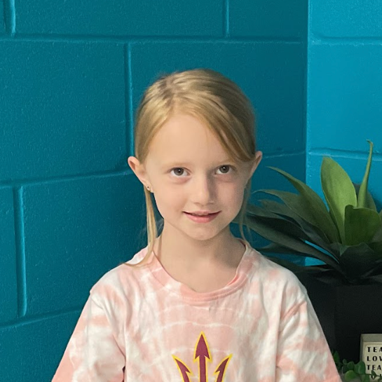 Cameron Seward wearing a pink tie dye shirt standing in front of a turquoise wall and plant