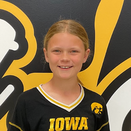 Rose Hammes, MP Middle School student wearing a black and gold shirt with the Iowa Hawk on it in front of the MP hawk wall decal