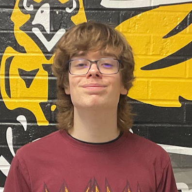 Parker Thomas wearing a burgundy shirt with Def Leppard text in gold standing in front of the MP hawk wall decal