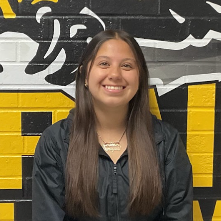 Maya wearing a black jacket standing in front of the MP hawk wall decal
