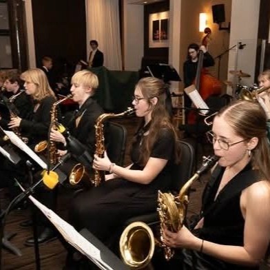 Jazz band students playing saxophones dressed in black outfits reading music on music stands