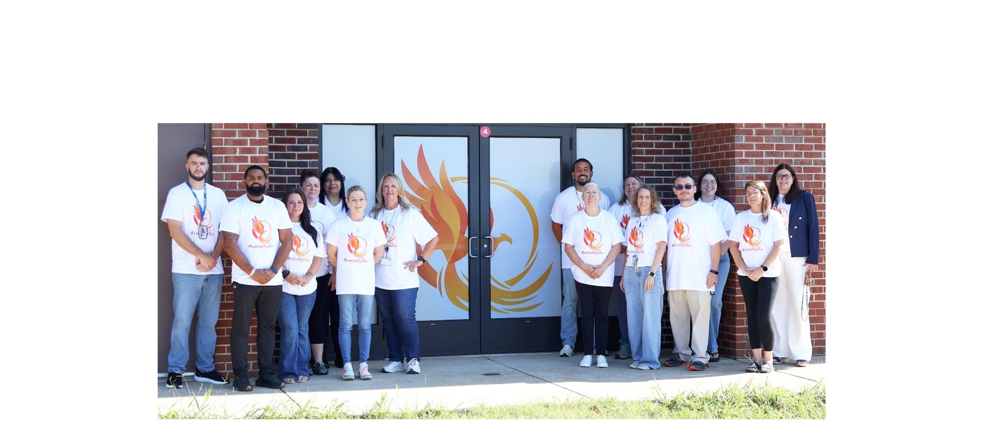 A group of people in matching white shirts stands in front of a brick building with an orange flame logo.