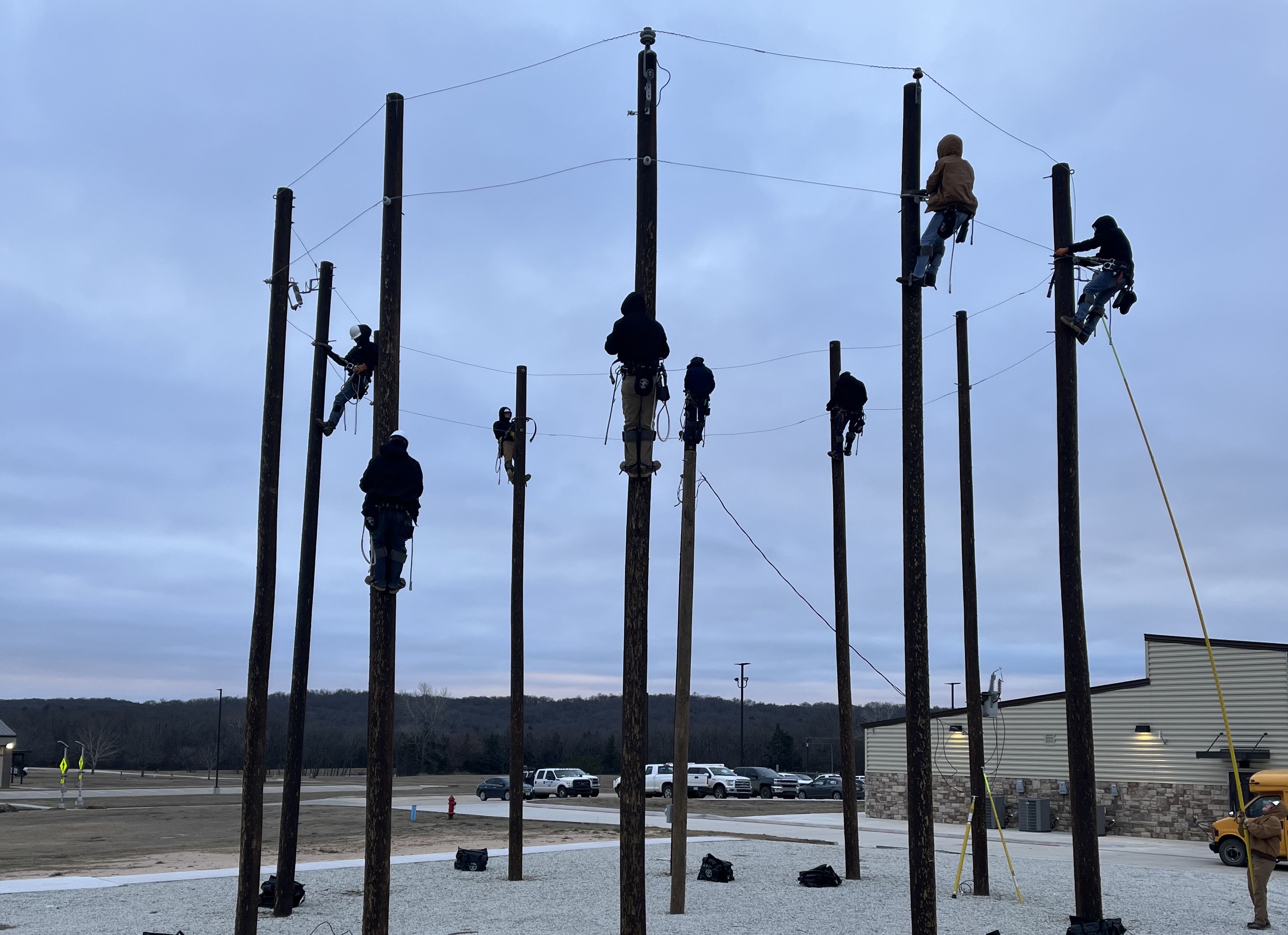 Several lineworker students climbing a circle of utility poles