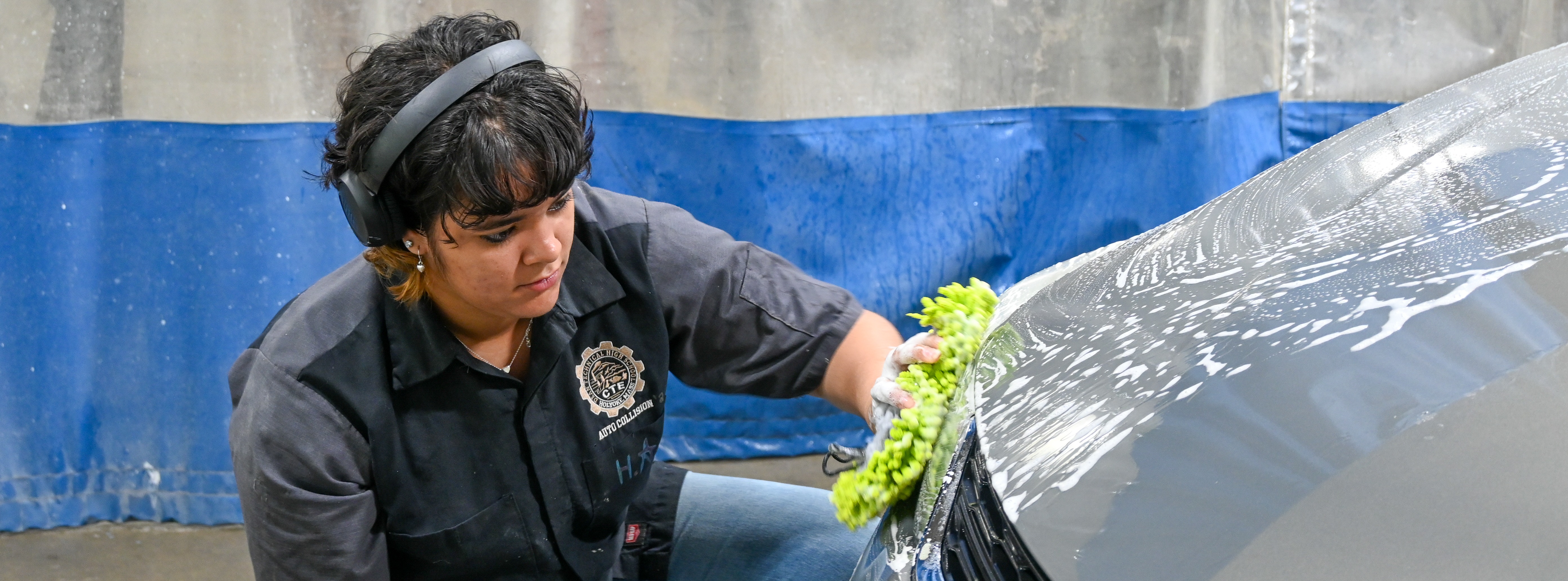 student bent down washing a car