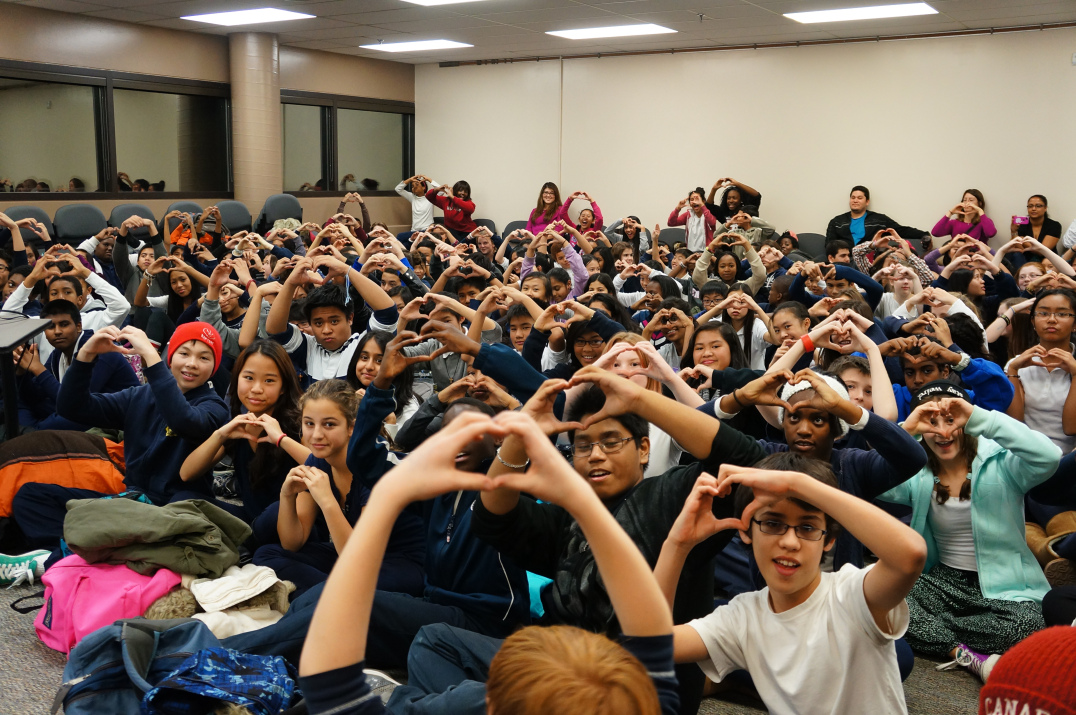 Group of elementary students making heart shapes with their hands at E-CSLIT general assembly