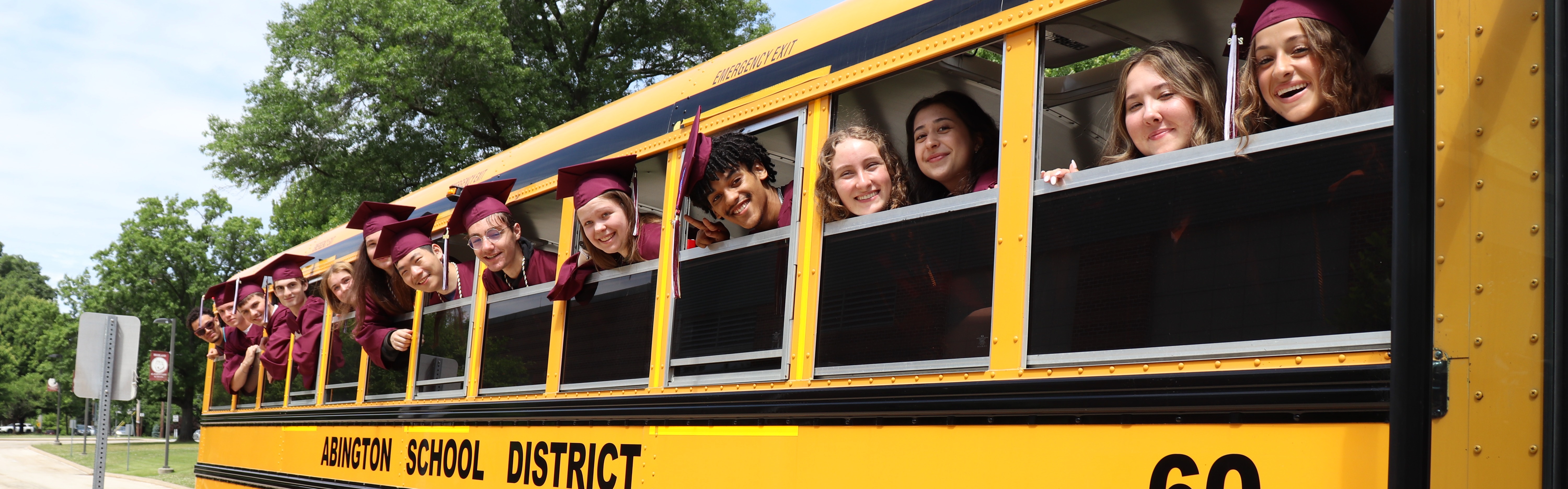 Students in caps and gowns stick their heads out of the windows of a school bus