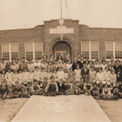A large historical group photo of students and teachers posed in rows outside a brick schoolhouse, dated 1928.