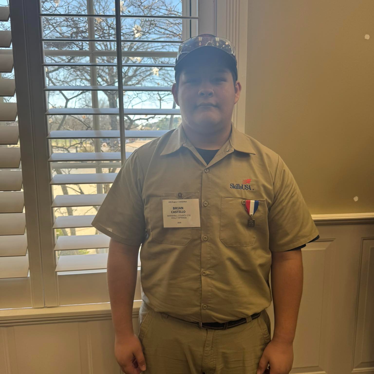 Brian Castillo standing by a window with his third place medal