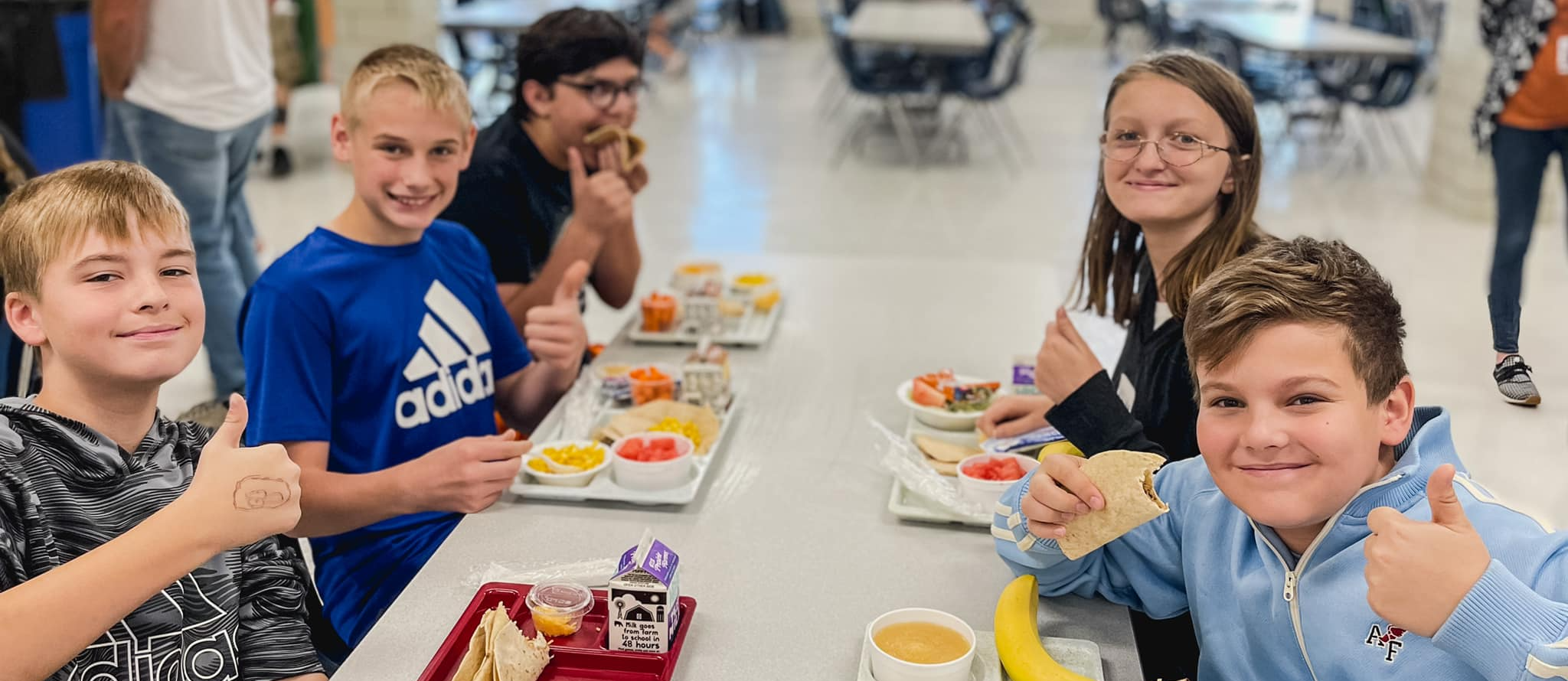 students at lunch giving camera a thumbs up