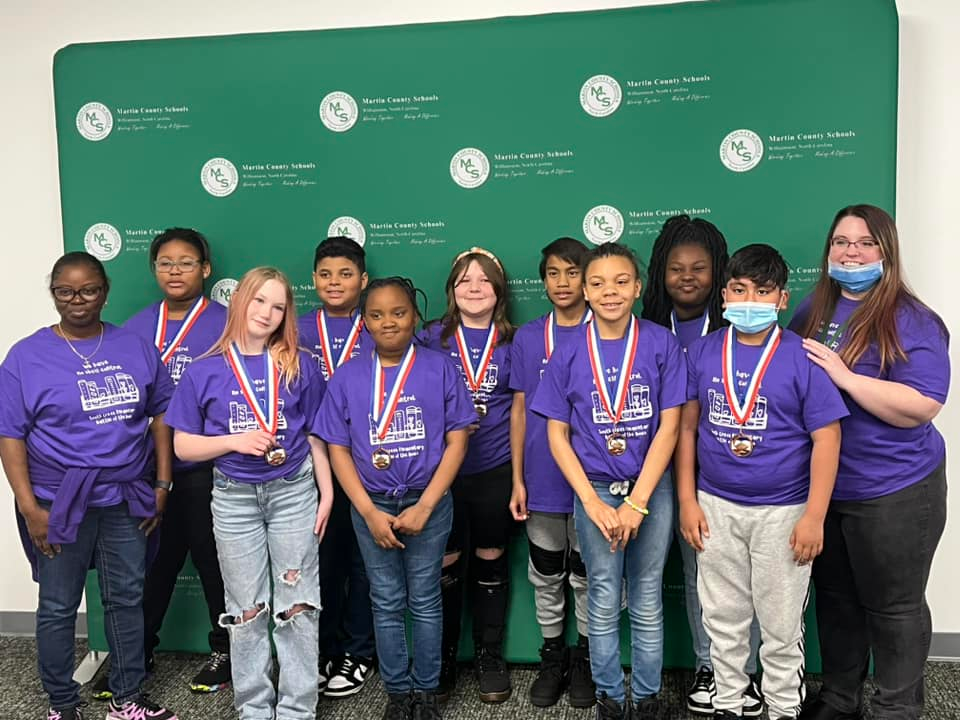 Students and coaches stand in front of green MCS screen post-competition