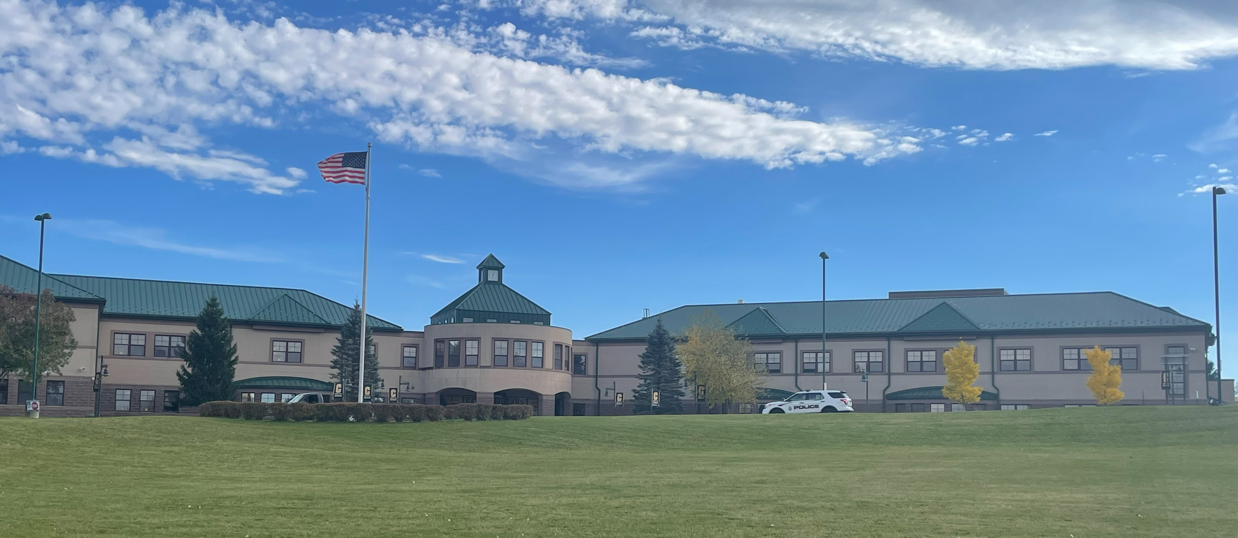 The Canajoharie High School is shown on sunny day with white clouds in a bright blue sky. The lawn of the building is visible in front of it. 